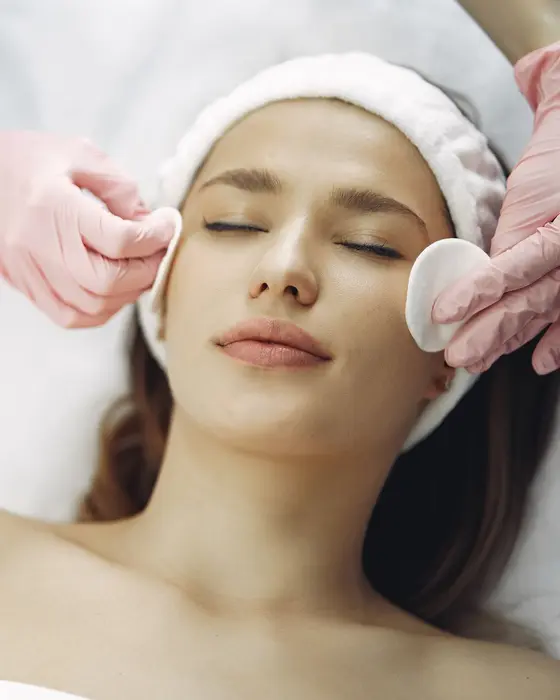 Esteticista limpando o rosto de uma cliente com discos de algodão